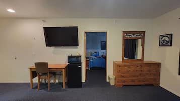 A hotel room with a desk, chair, dresser, TV, and two beds.