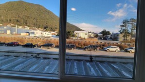 Vista desde una ventana sobre un estacionamiento con varios autos, un edificio y una montaña al fondo.
