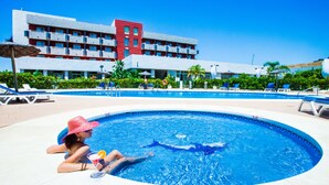 A swimming pool with lounge chairs and umbrellas, a building with multiple balconies, and lush greenery in the background. - Montera Plaza (Los Barrios)