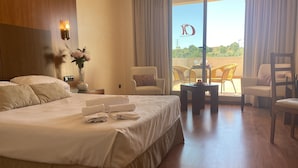 A hotel room with a large bed, two armchairs, a small table, and a balcony with wicker chairs. - Montera Plaza (Los Barrios)