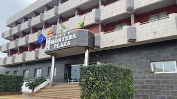 A multi-story building with balconies, a sign reading "Montera Plaza," and flags.