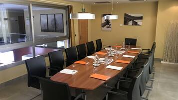 Un salón de conferencias con una larga mesa, sillas negras y cristalería.