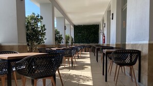 An outdoor covered patio with multiple tables and chairs, a fire extinguisher, and a wall with greenery. - Montera Plaza (Los Barrios)