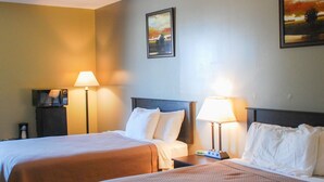A hotel room with two beds, each with a pillow and a blanket, a nightstand with a lamp, and a painting on the wall. - Sunlac Inn (Lakota)