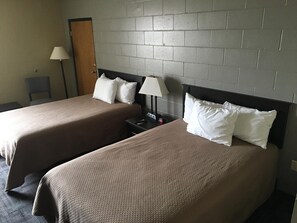 A hotel room with two beds, a nightstand, a lamp, and a chair.