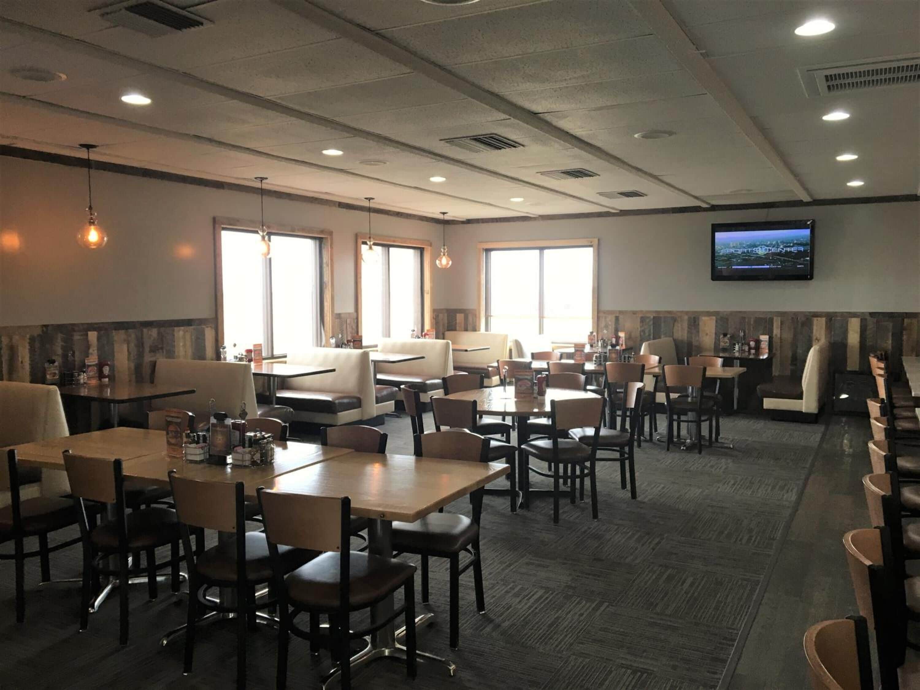 Ein Restaurant mit Sitzgelegenheiten in Form von Boxen und Tischen, großen Fenstern und einem Fernseher an der Wand.
