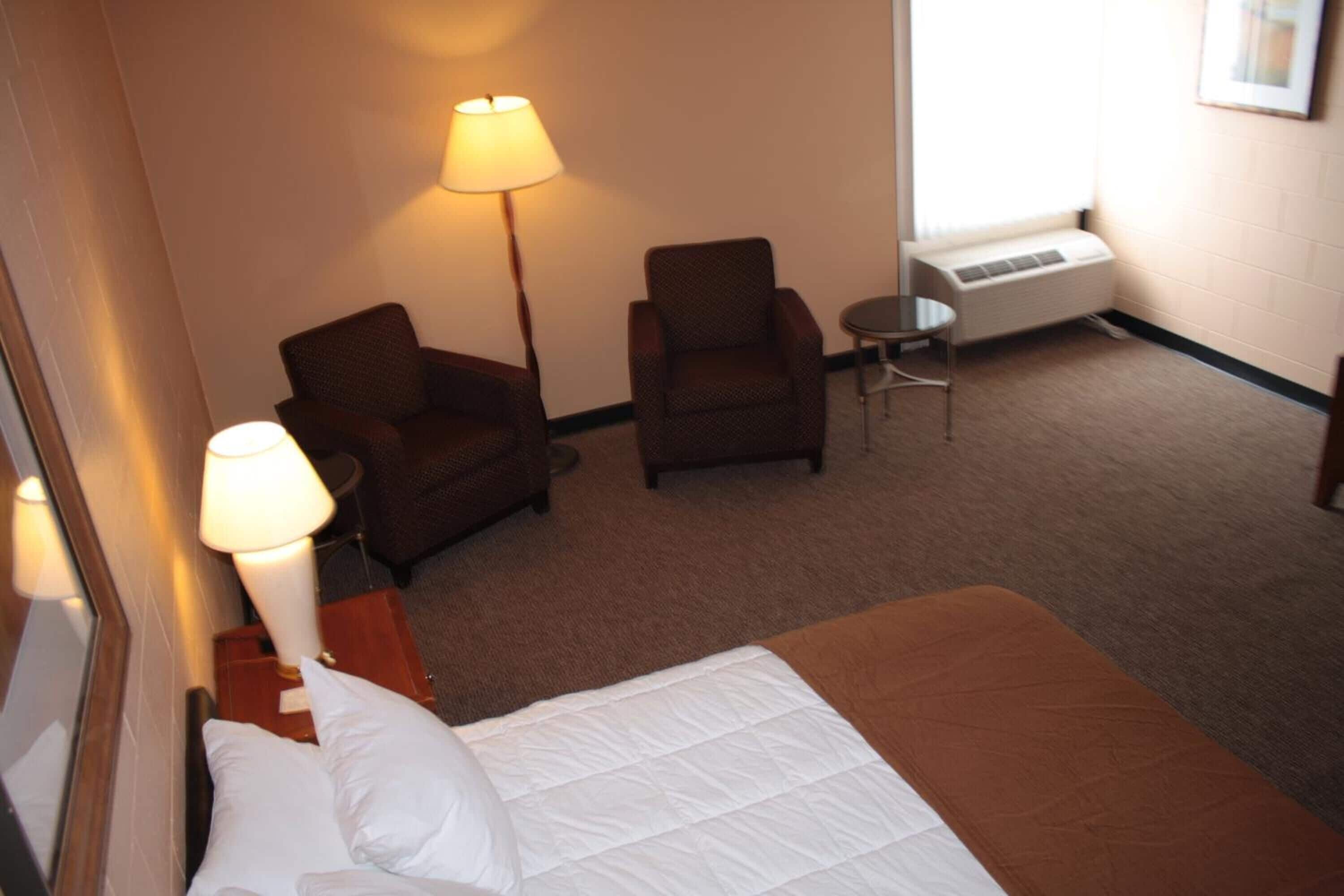 Una habitación de hotel con una cama, dos sillones, una mesita, una lámpara y un radiador.