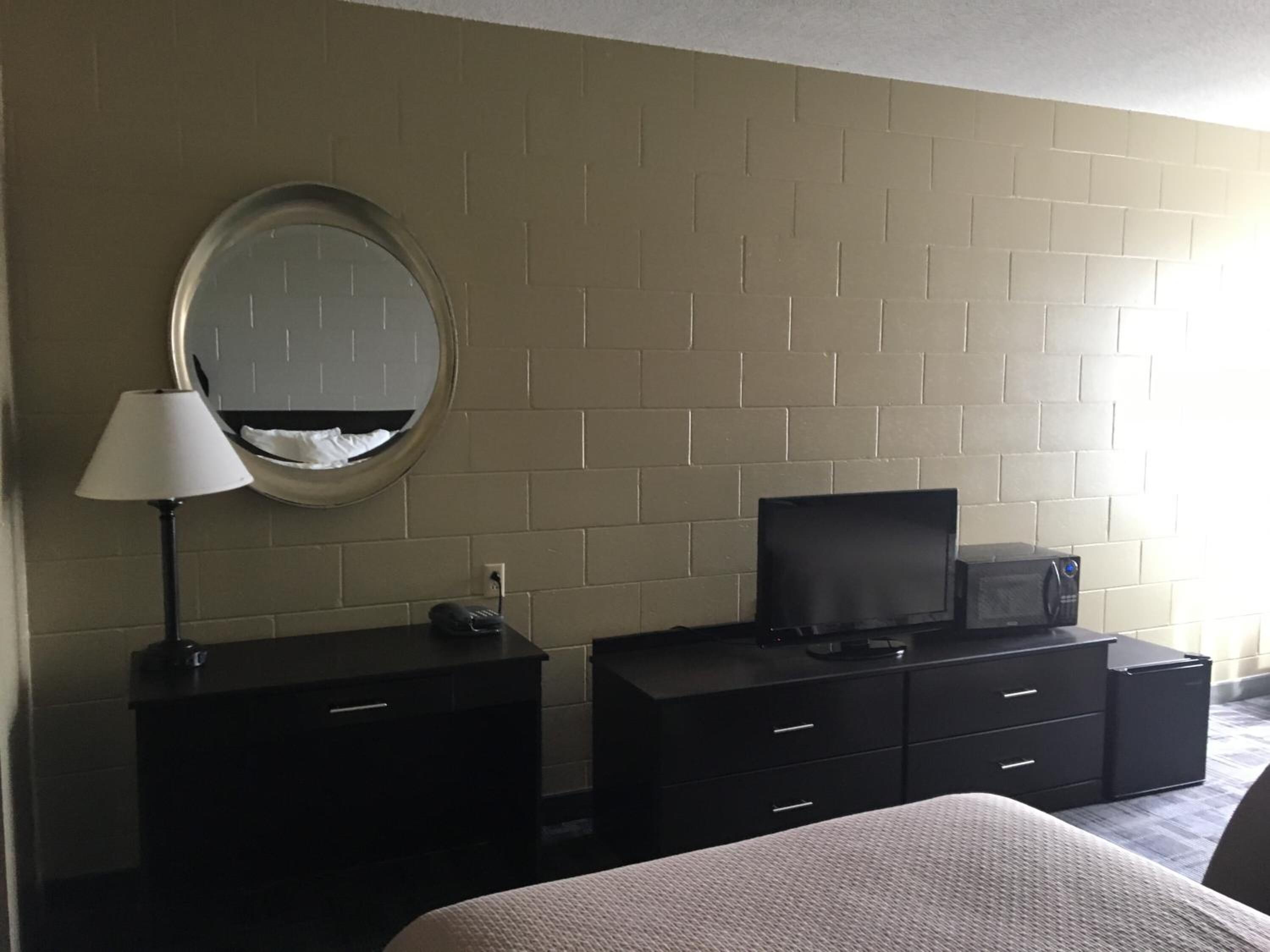 Una habitación de hotel con cama, cómoda, televisor y espejo en la pared.