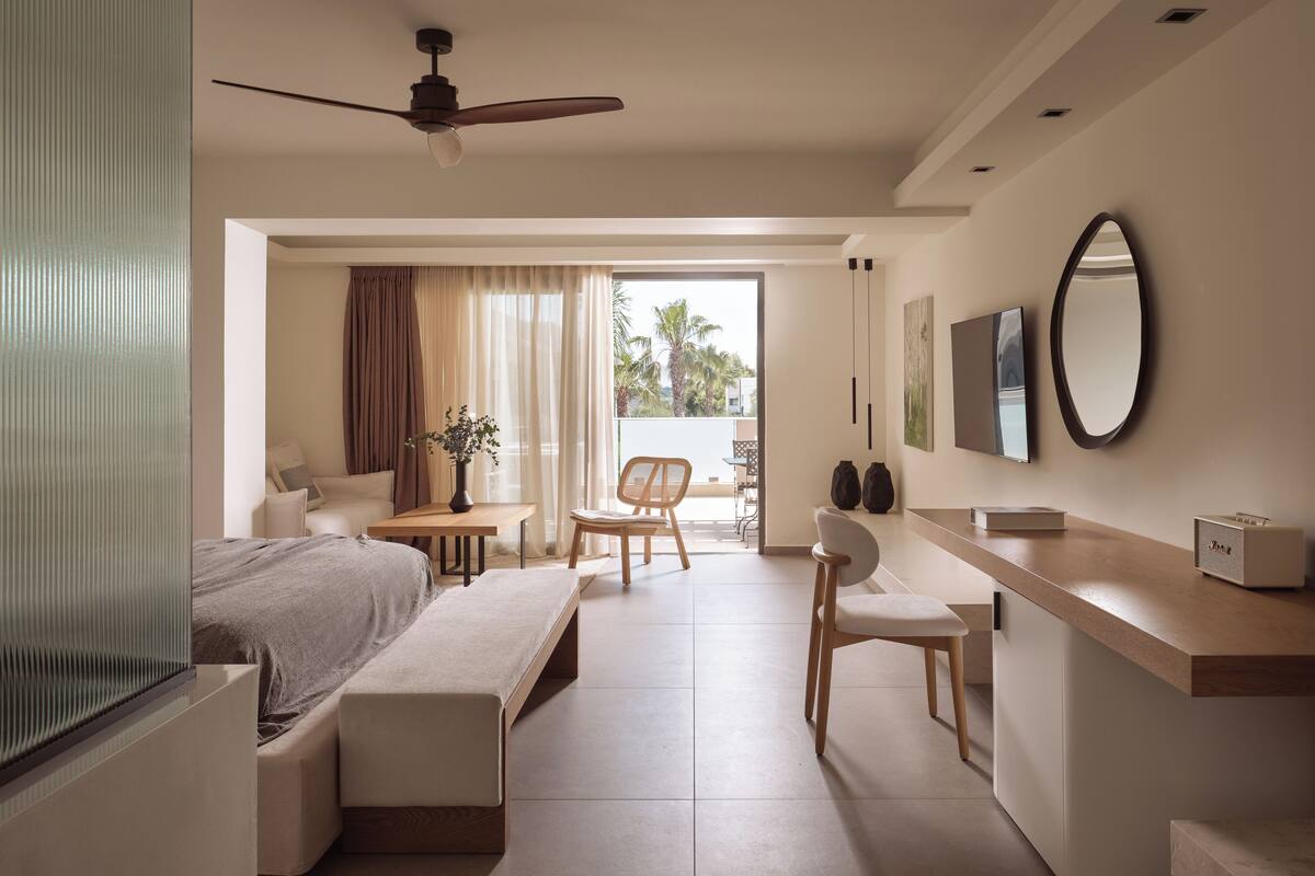 Une chambre d’hôtel moderne équipée d’un lit, d’un bureau, d’une chaise, d’un banc, d’un ventilateur de plafond et d’un balcon avec des rideaux.