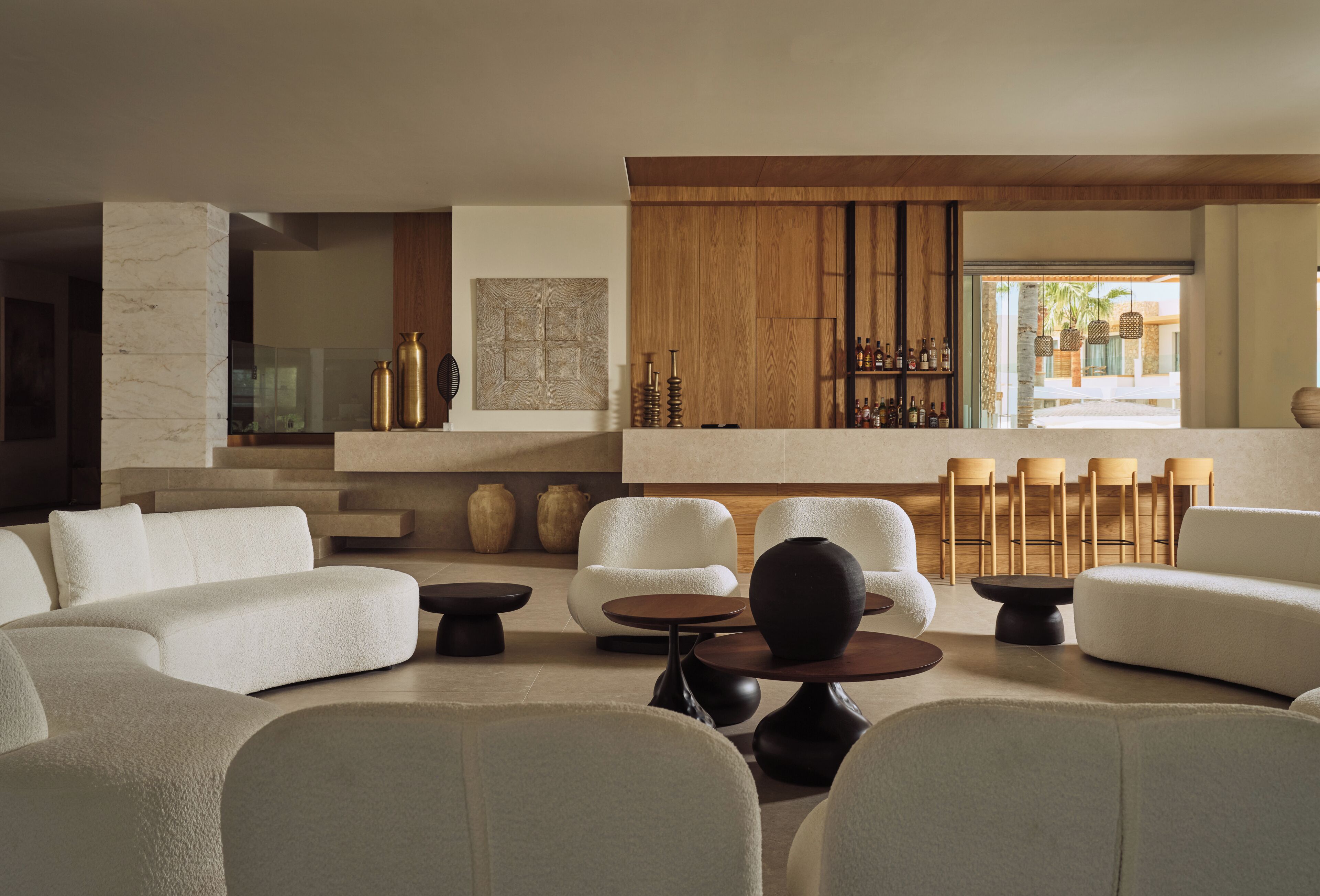 Una sala de estar moderna con sofás blancos, una mesa de centro y una zona de bar con sillas de madera.