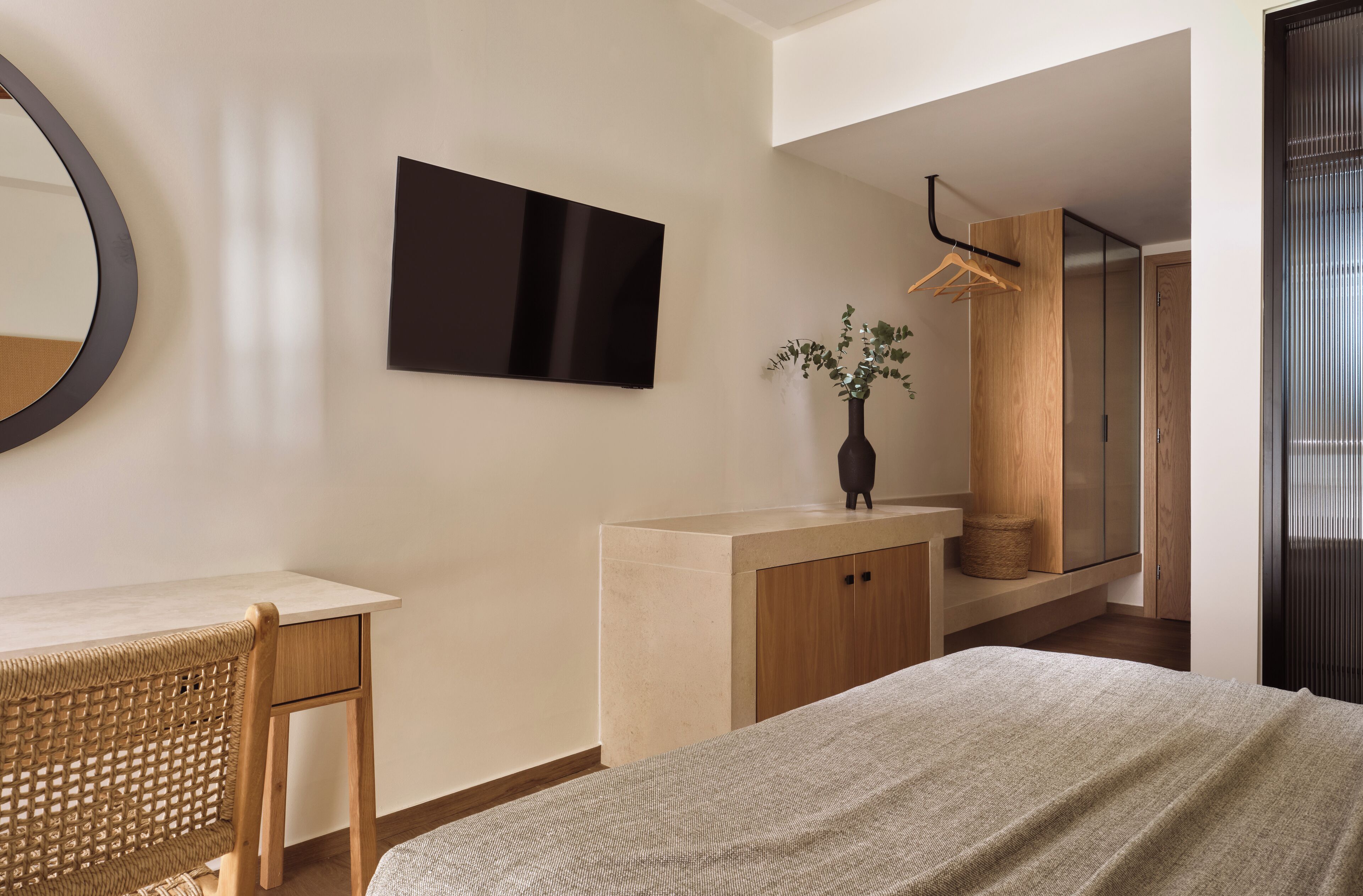 A modern bedroom with a bed, a desk, a chair, a TV, and a wardrobe.