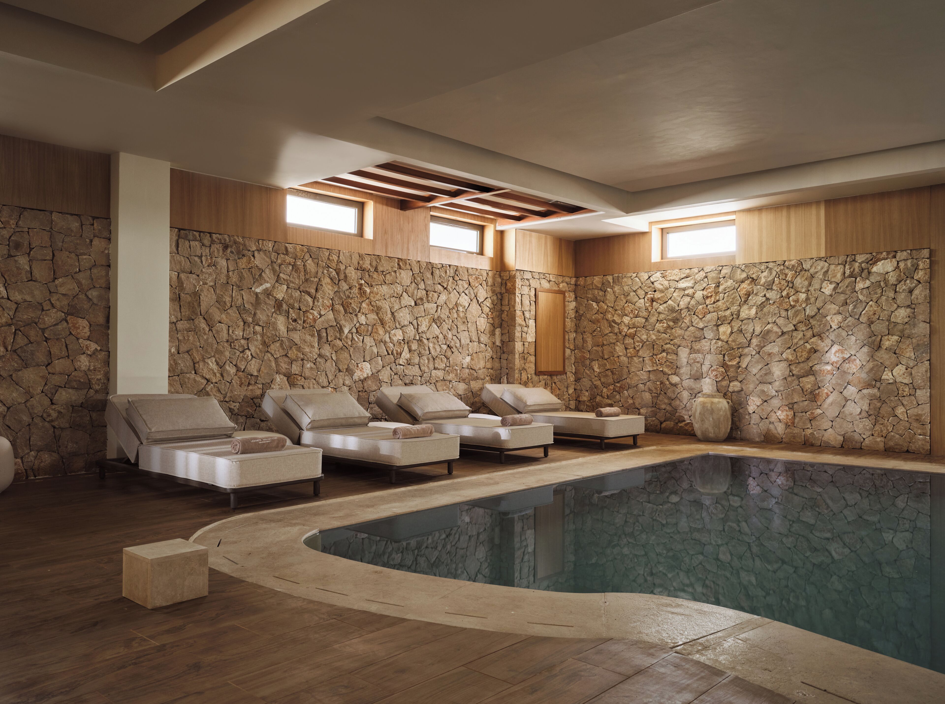 A spa area with stone walls, a pool, and lounge chairs.