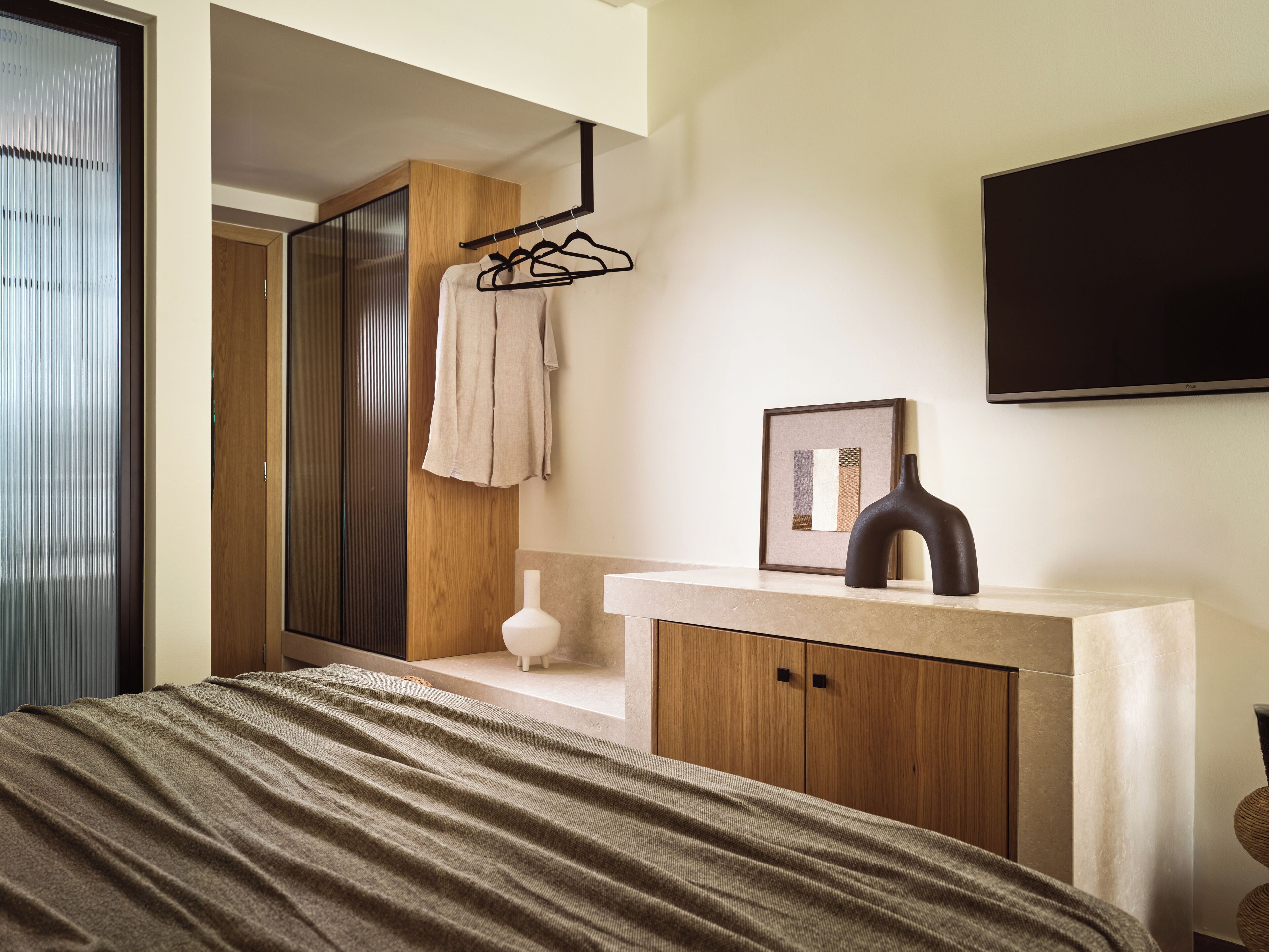 Una camera da letto moderna con un letto, un armadio in legno, un bagno con porta asciugamani, un quadro incorniciato e un televisore a parete.