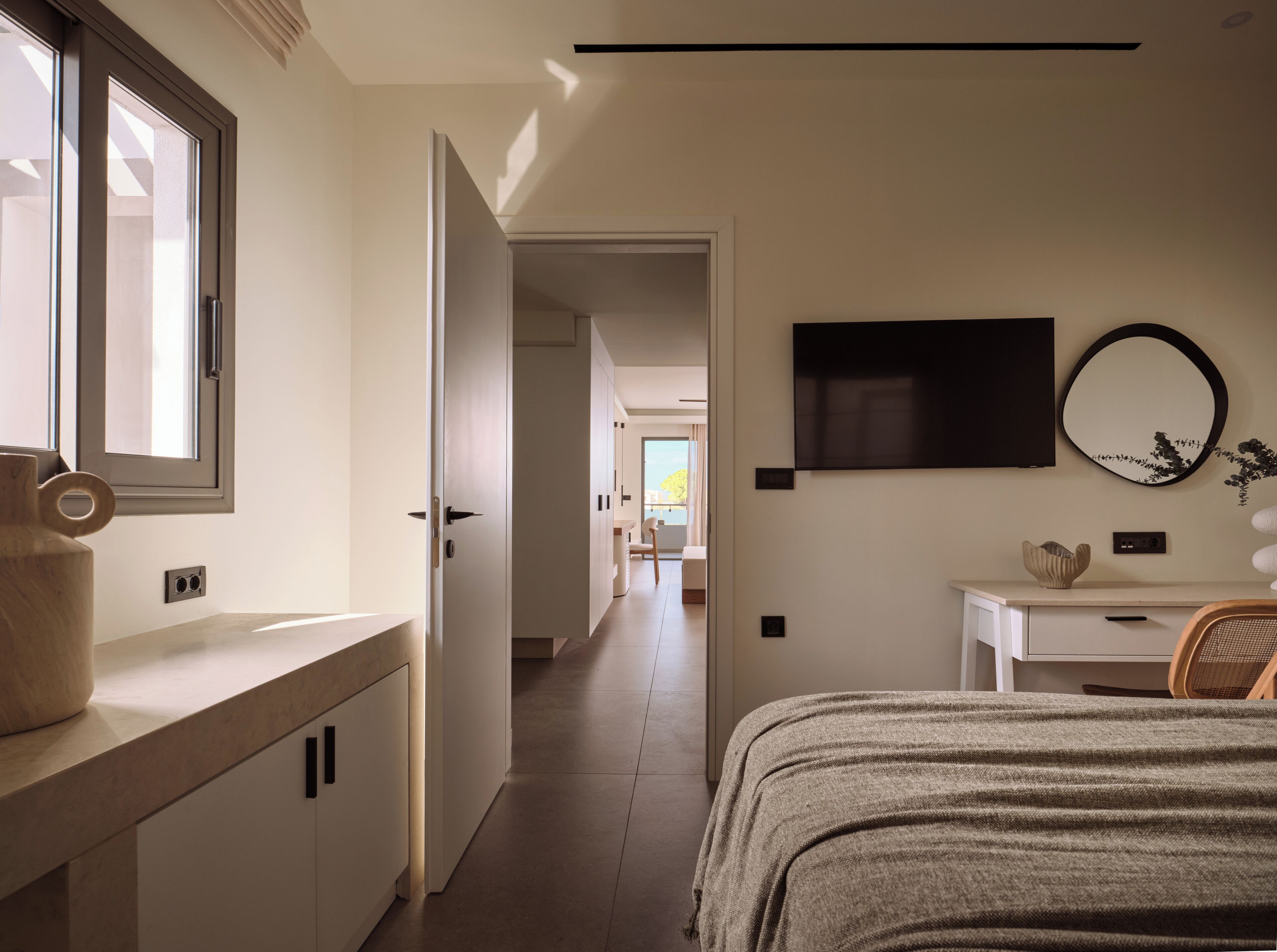Un dormitorio moderno con una cama, un televisor, un espejo y una ventana.