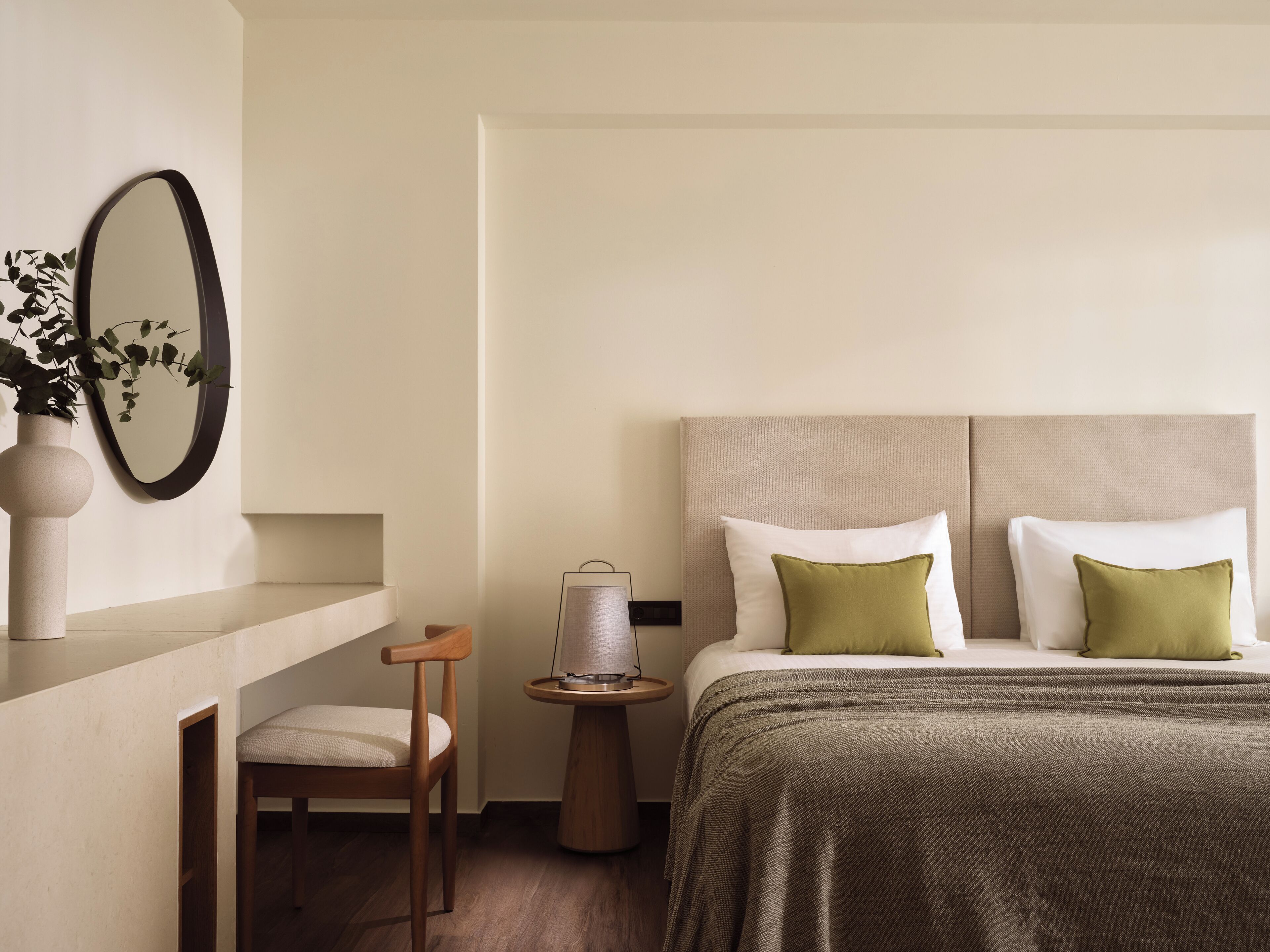 A hotel room with a bed, bedside table, chair, and a wall-mounted mirror.