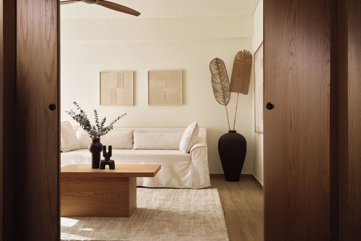 Un salon moderne avec un plancher en bois, un canapé blanc, une table basse en bois et un vase noir orné de branches décoratives.