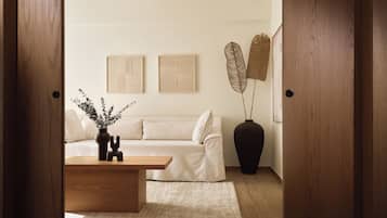 Un soggiorno moderno con pavimento in legno, un divano bianco, un tavolino in legno e un vaso nero con rami decorativi.