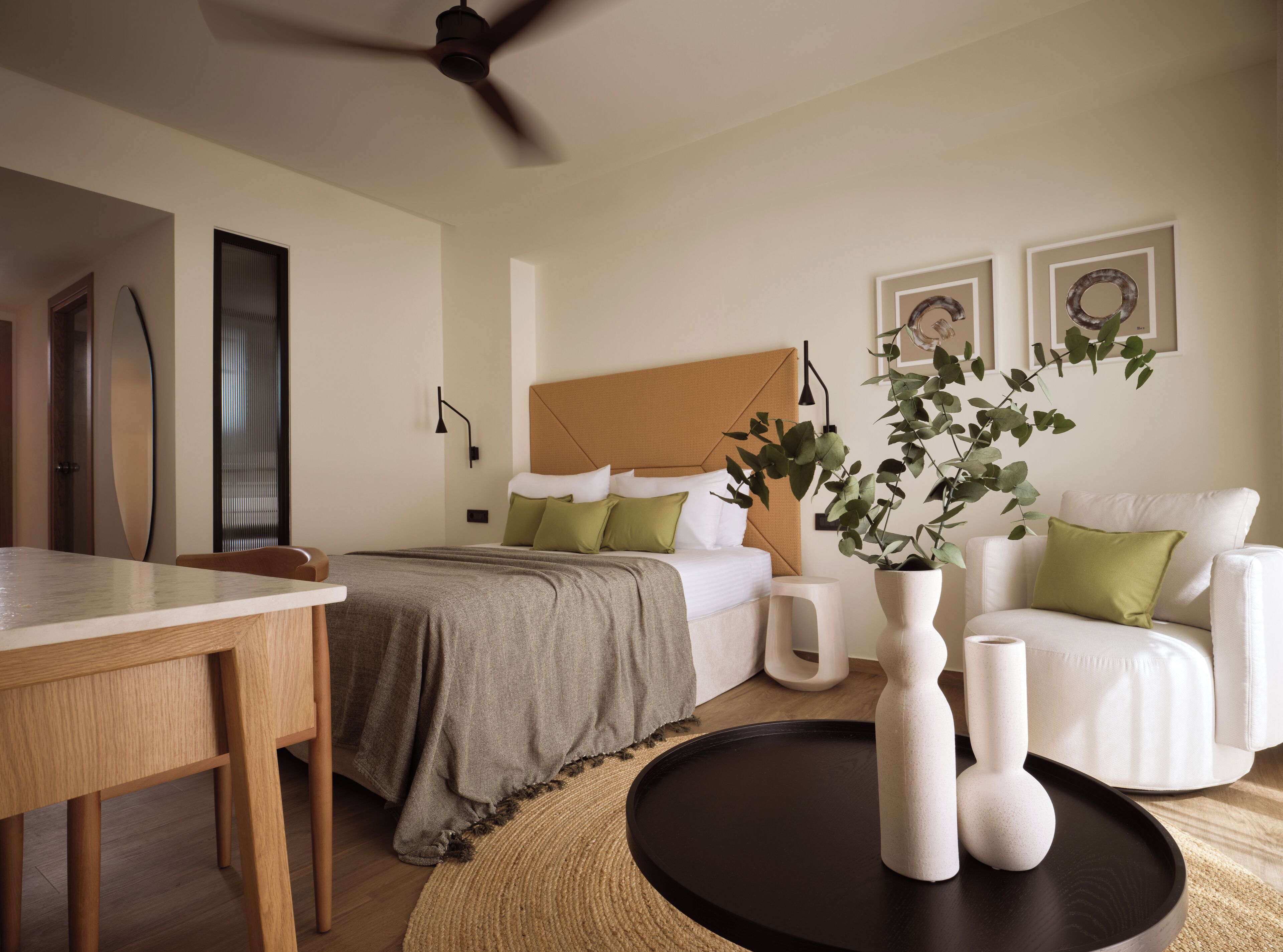 A modern bedroom with a bed, bedside tables, a chair, a dining table, and a ceiling fan.