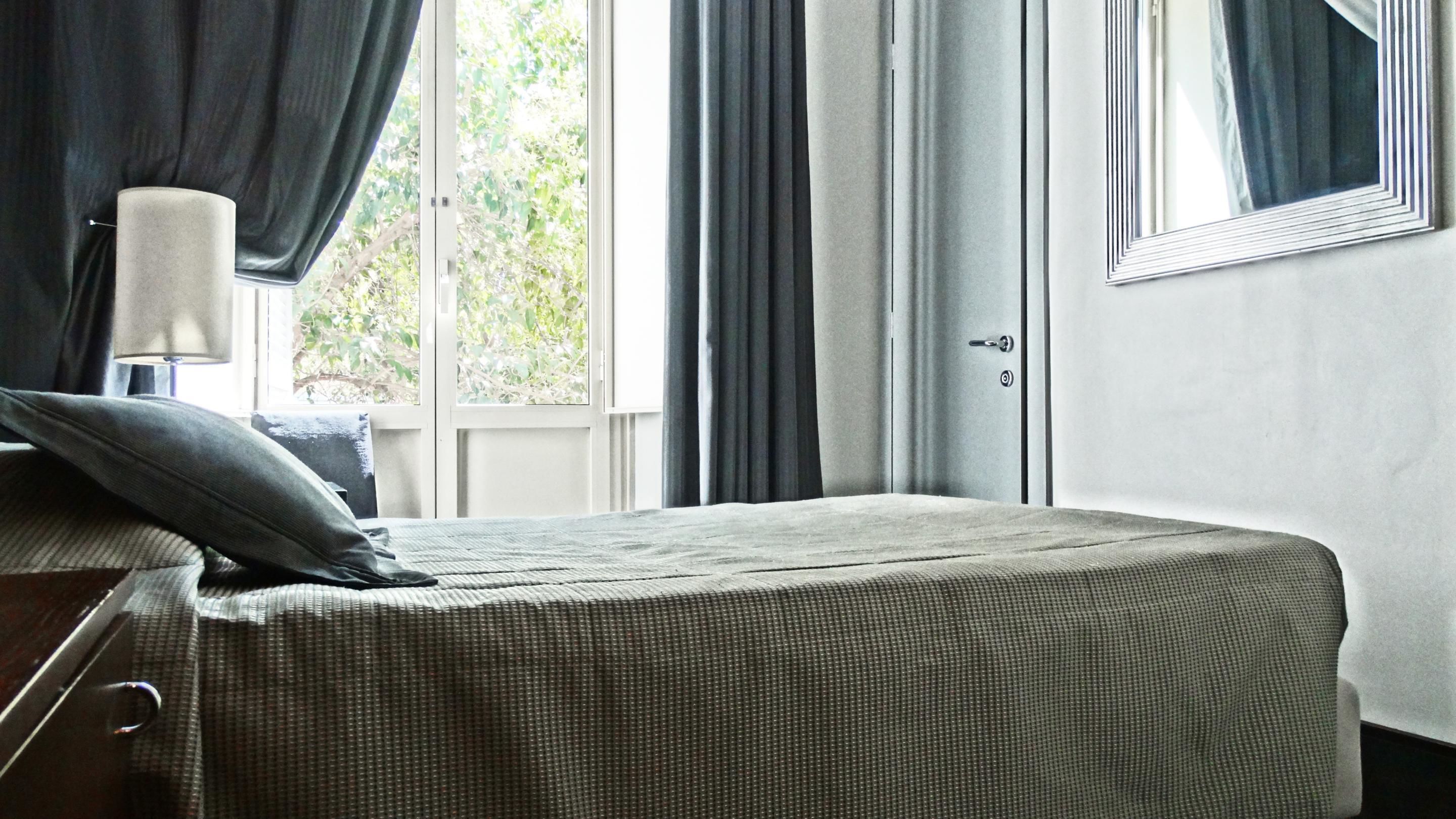 A bedroom with a bed, a nightstand, a lamp, and a window with curtains.