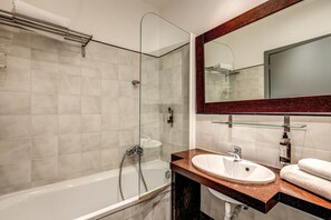Een moderne badkamer met een douchecabine van glas, een witte wastafel en een houten opbergmeubel.