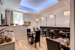 Een restaurant met een hoge plafond, hanglampen en een zithoek met tafels en stoelen.
