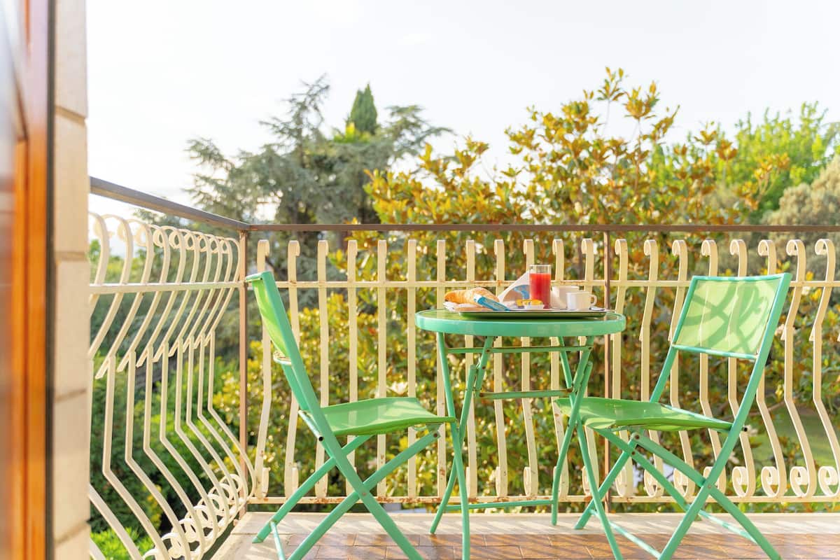 A balcony with a green metal table and chairs, a small table with a cup and a glass, and a white metal railing.