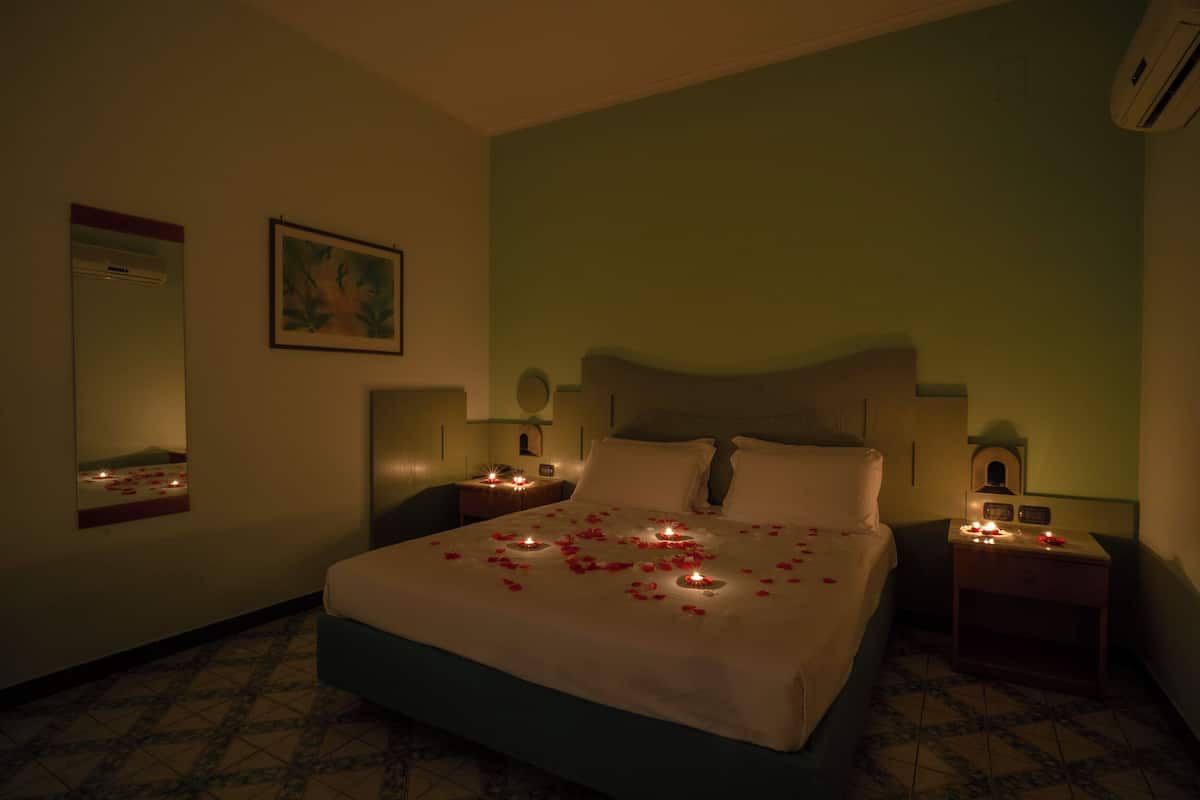 A hotel room with a bed, bedside lamps, a nightstand, a mirror, and a wall-mounted air conditioner.