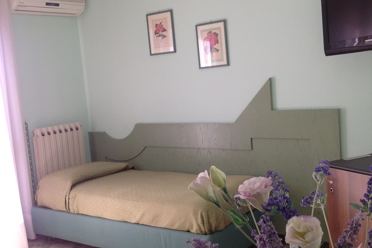 A bedroom with a bed, a radiator, a wall-mounted TV, and framed pictures.