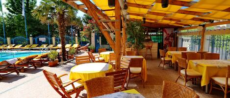An outdoor seating area with tables and chairs, a pool, and a covered section with umbrellas.