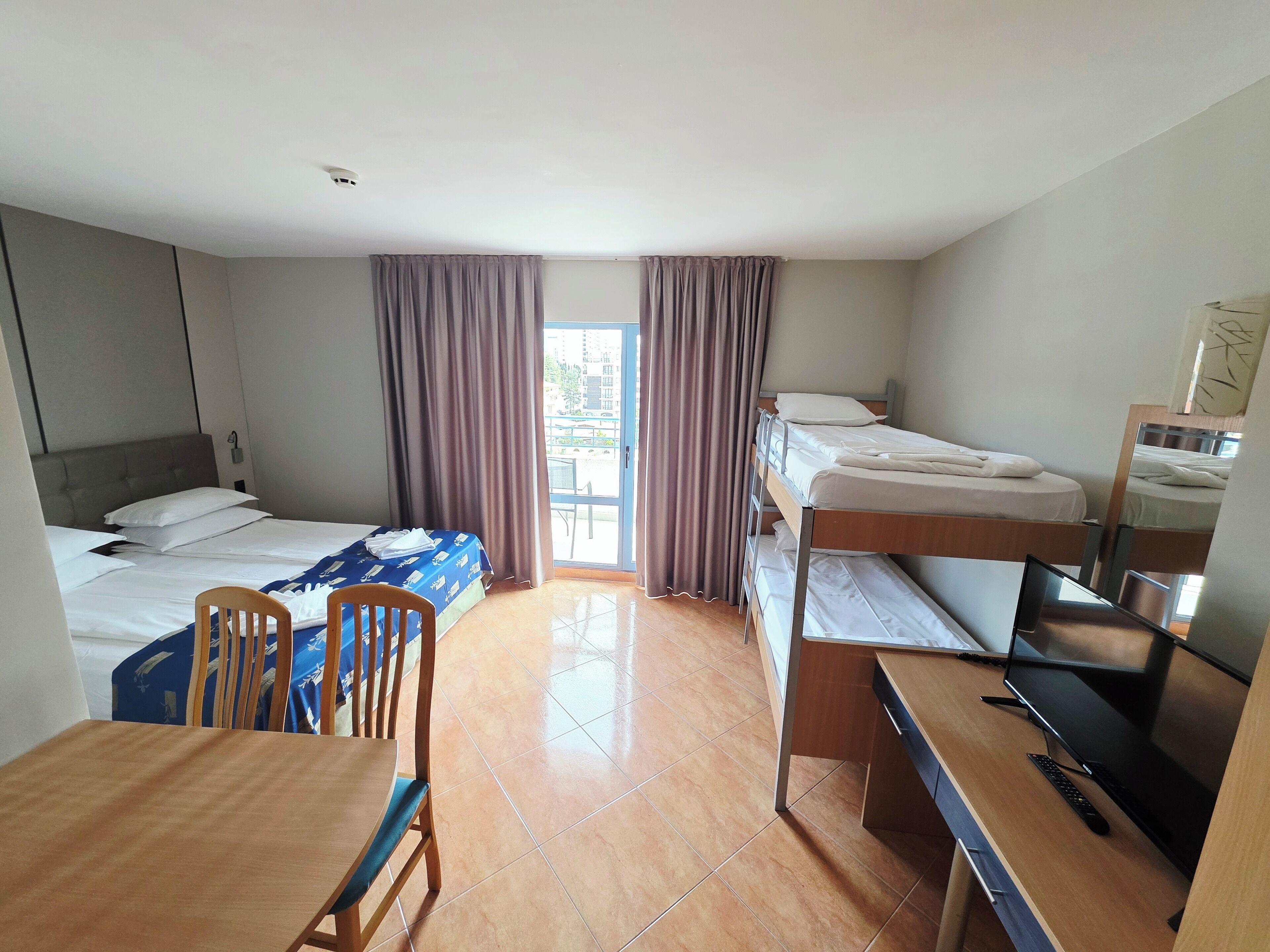 A hotel room with a single bed, a desk with a computer, a chair, and a bunk bed.