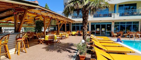 A poolside area with yellow lounge chairs and a bar area with wooden furniture and a tiled floor.