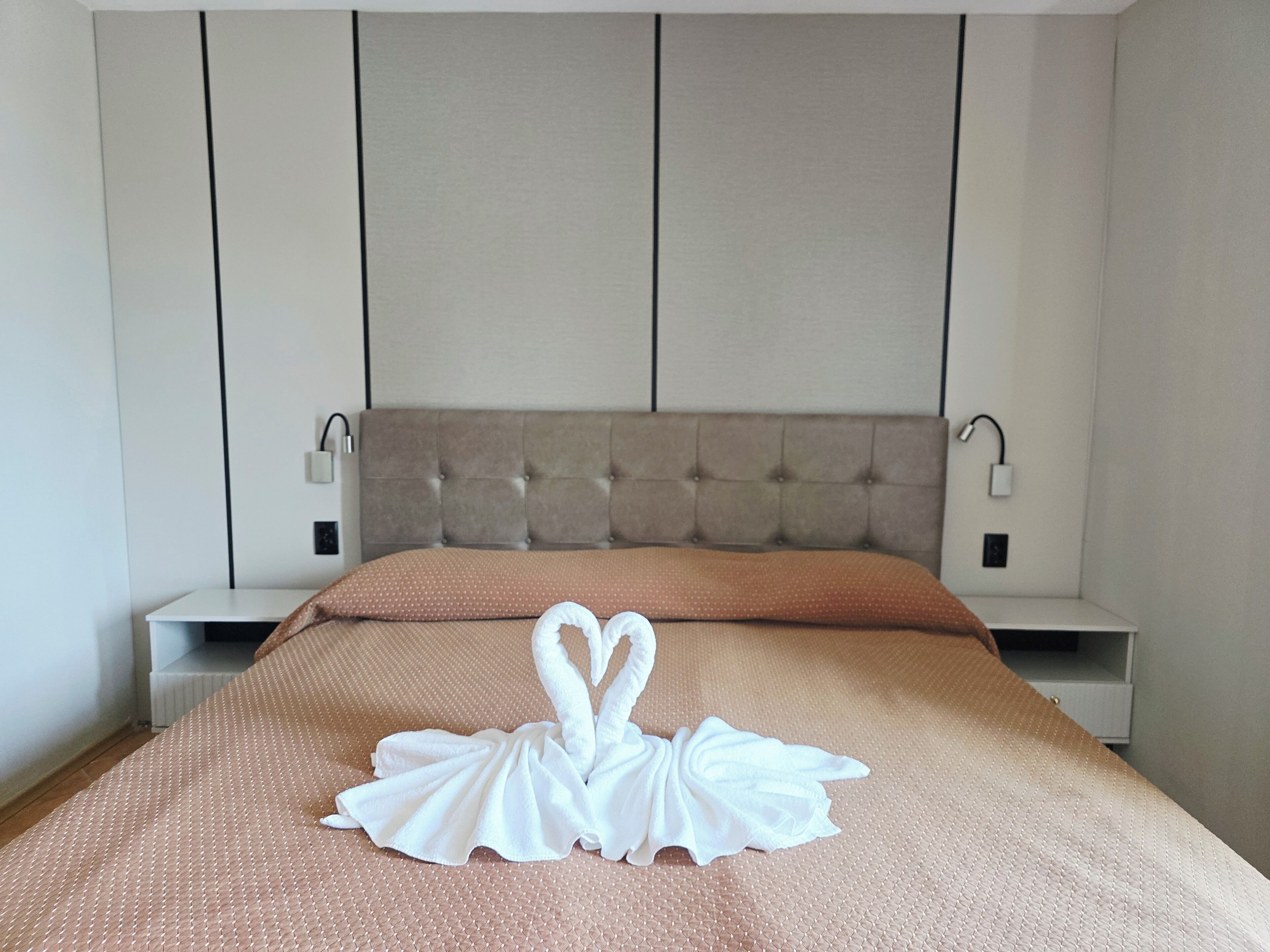 Una cama bien hecha con una colcha marrón y dos toallas blancas dispuestas en forma de cisne.