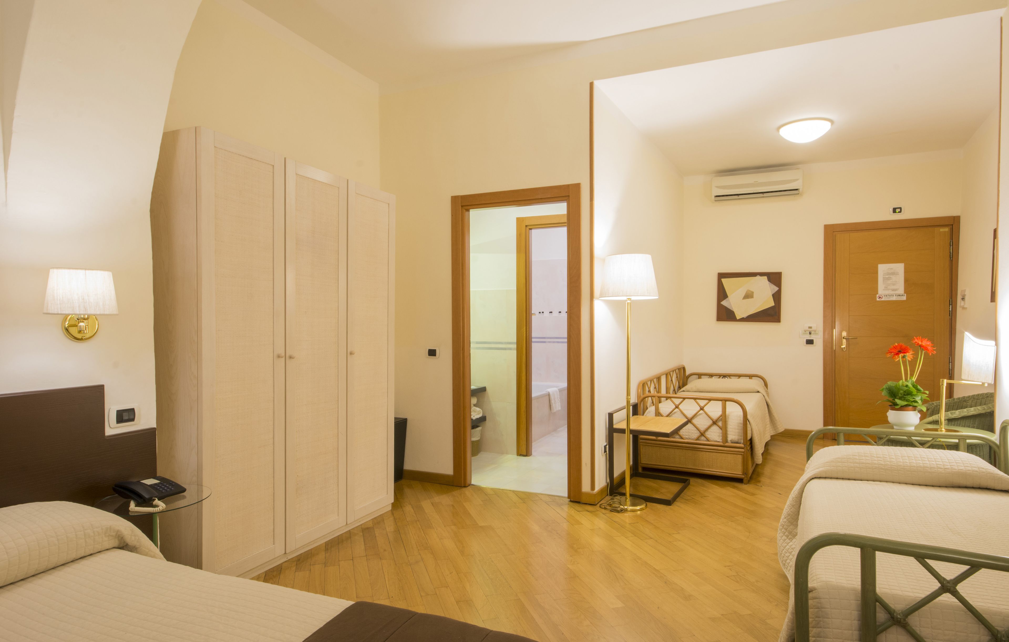 A hotel room with a bed, a desk with a lamp, a wardrobe, and a bathroom visible through an open door.