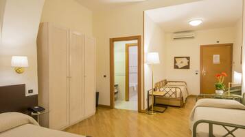 A hotel room with a bed, a desk with a lamp, a wardrobe, and a bathroom visible through an open door.