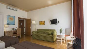 Habitación de hotel con un sofá verde a rayas, un escritorio con lámpara, televisión y una planta en maceta.