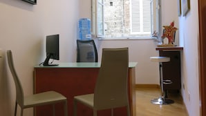 A small office with a desk, two chairs, a computer monitor, a water dispenser, and a window with a view of a brick building. - Piazza Paradiso Accomodation (Siena)