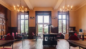 A spacious room with wooden floors, multiple tables and chairs, large windows, and chandeliers. - Domaine du Château de la Neuville (Huy)
