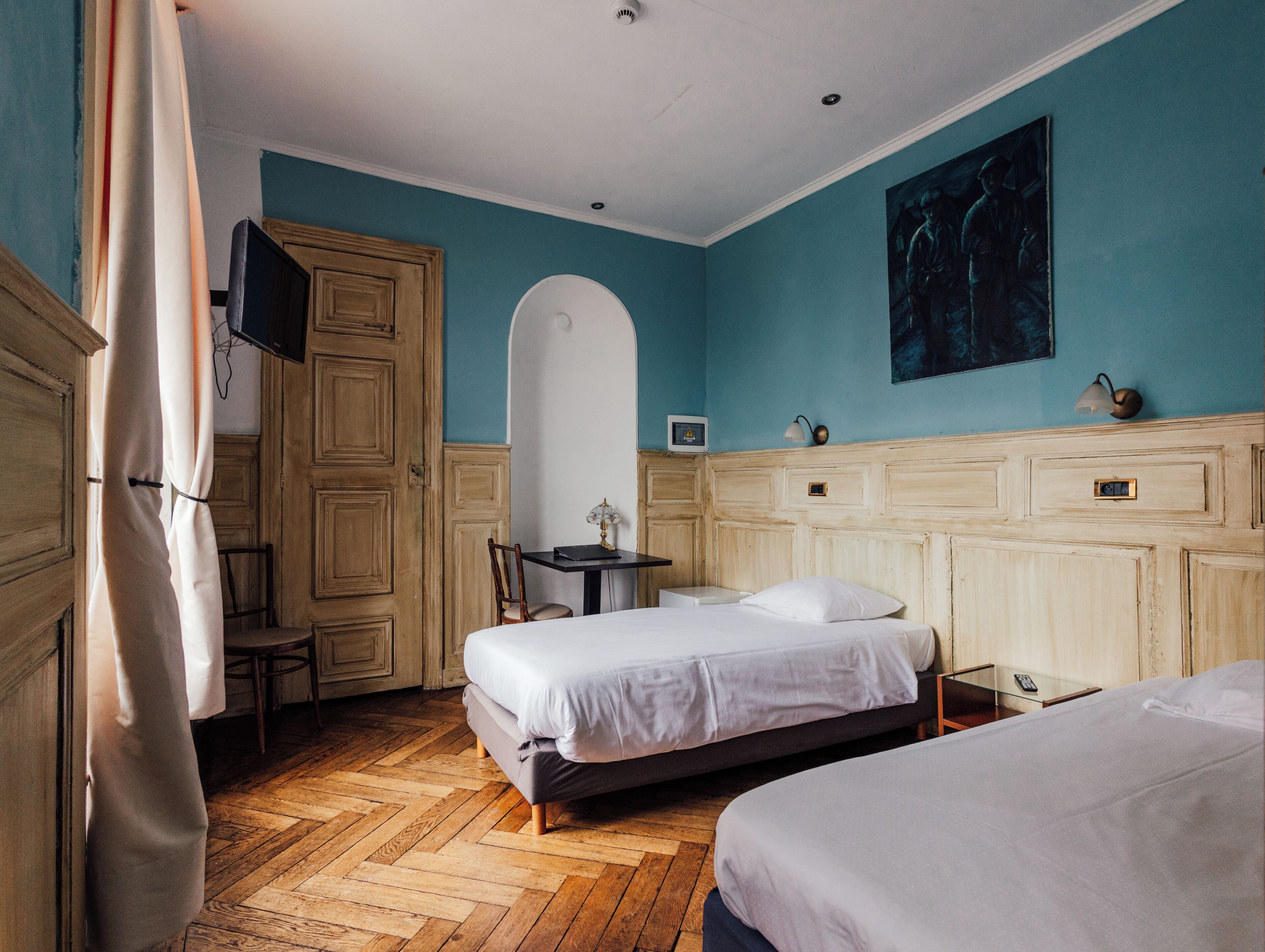 Habitación de hotel con dos camas, un escritorio, una silla, un televisor y un cuadro en la pared.