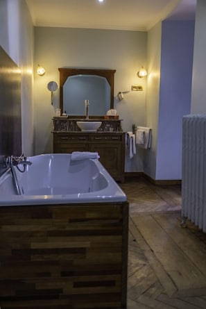 A bathroom with a wooden bathtub, a sink with a mirror, and a radiator. - Domaine du Château de la Neuville (Huy)