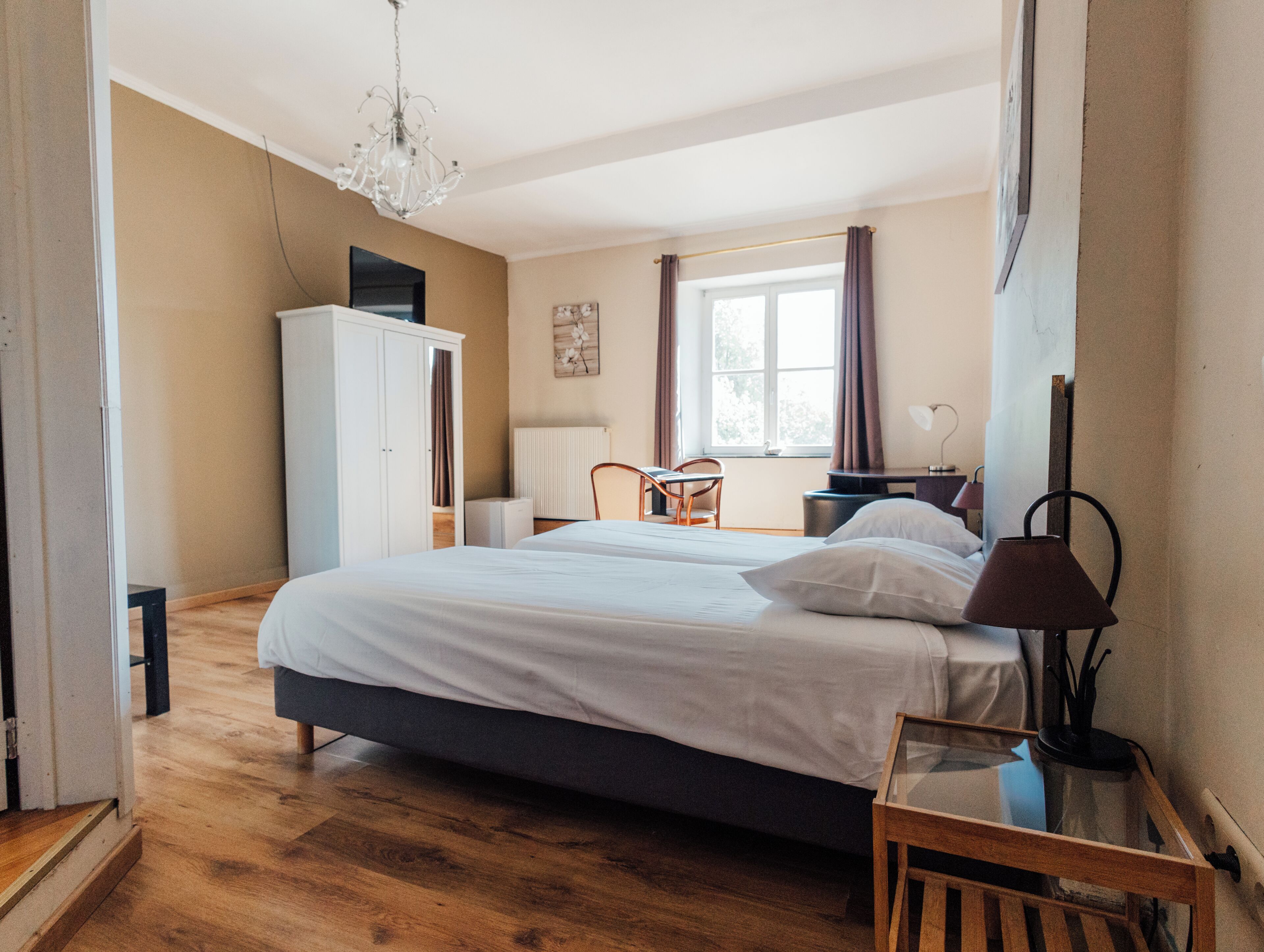 A bedroom with a bed, a desk, a chair, a wardrobe, and a window with curtains.