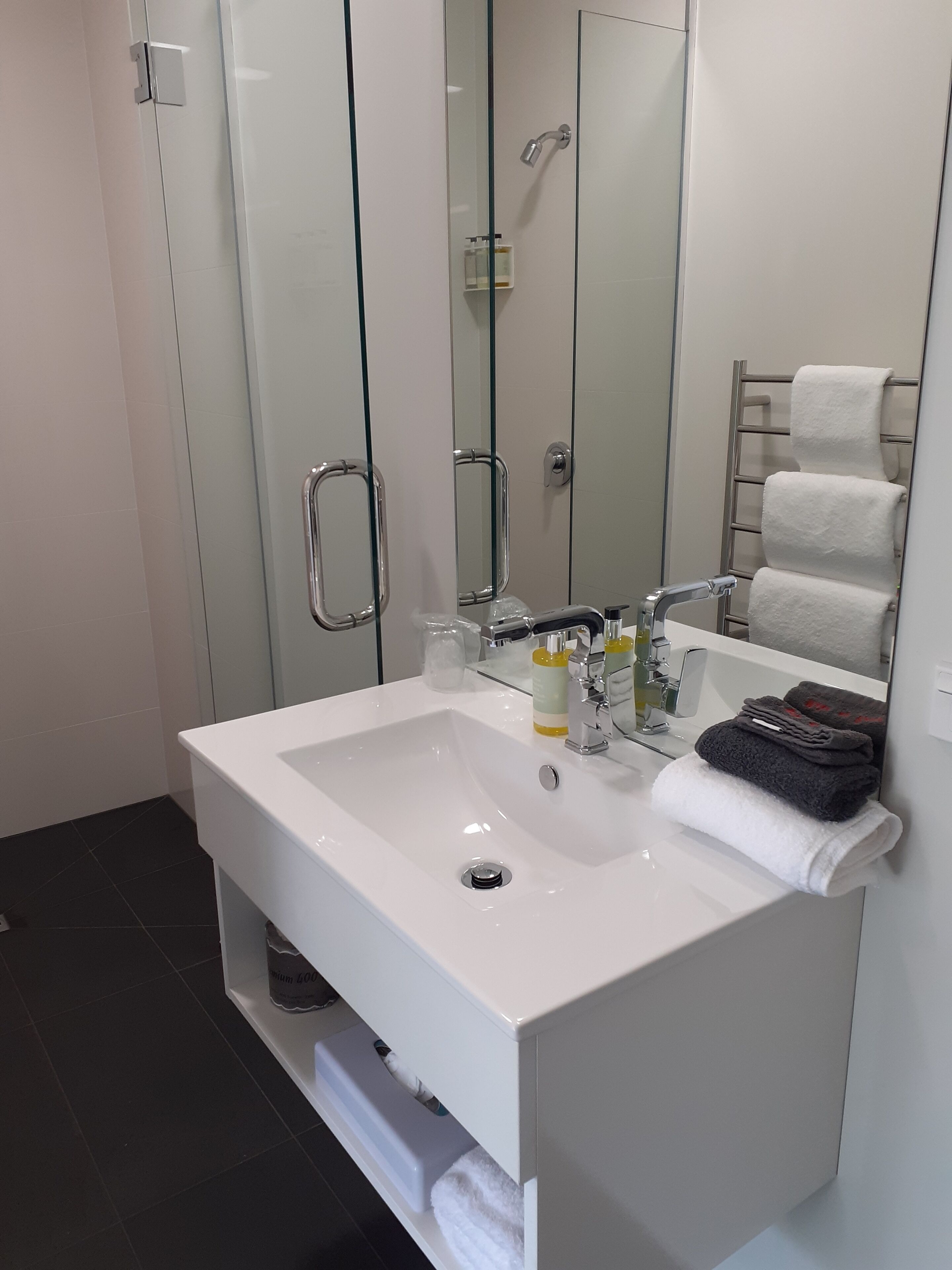 Un baño moderno con un lavamanos blanco, cabina de ducha con mampara de vidrio y un toallero con toallas dobladas.