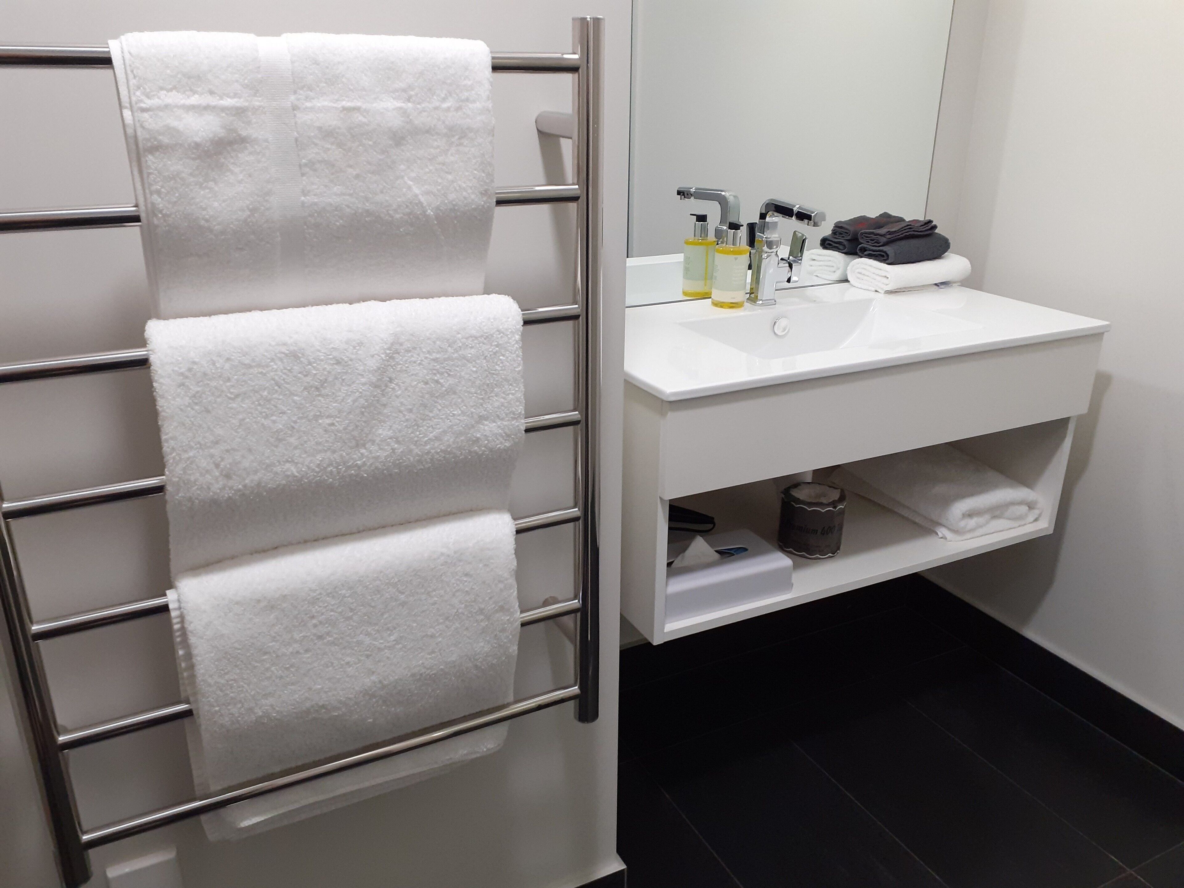 Een badkamer met een handdoekhouder met vier handdoeken, een witte wastafel met toiletartikelen en een spiegel.