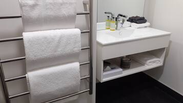 Een badkamer met een handdoekhouder met vier handdoeken, een witte wastafel met toiletartikelen en een spiegel.