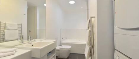 A modern bathroom with a large mirror, two sinks, a toilet, and a bathtub.