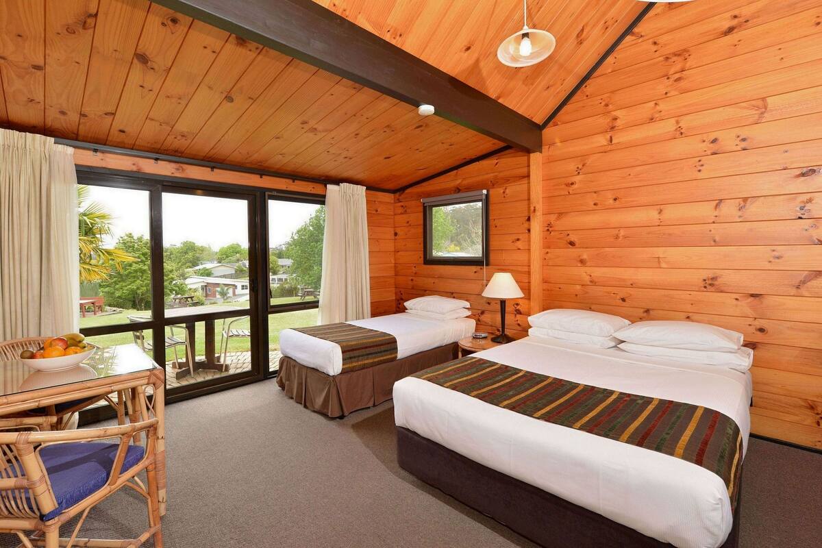 Een houten kamer met twee bedden, een tafel met fruit en uitzicht op de natuur.