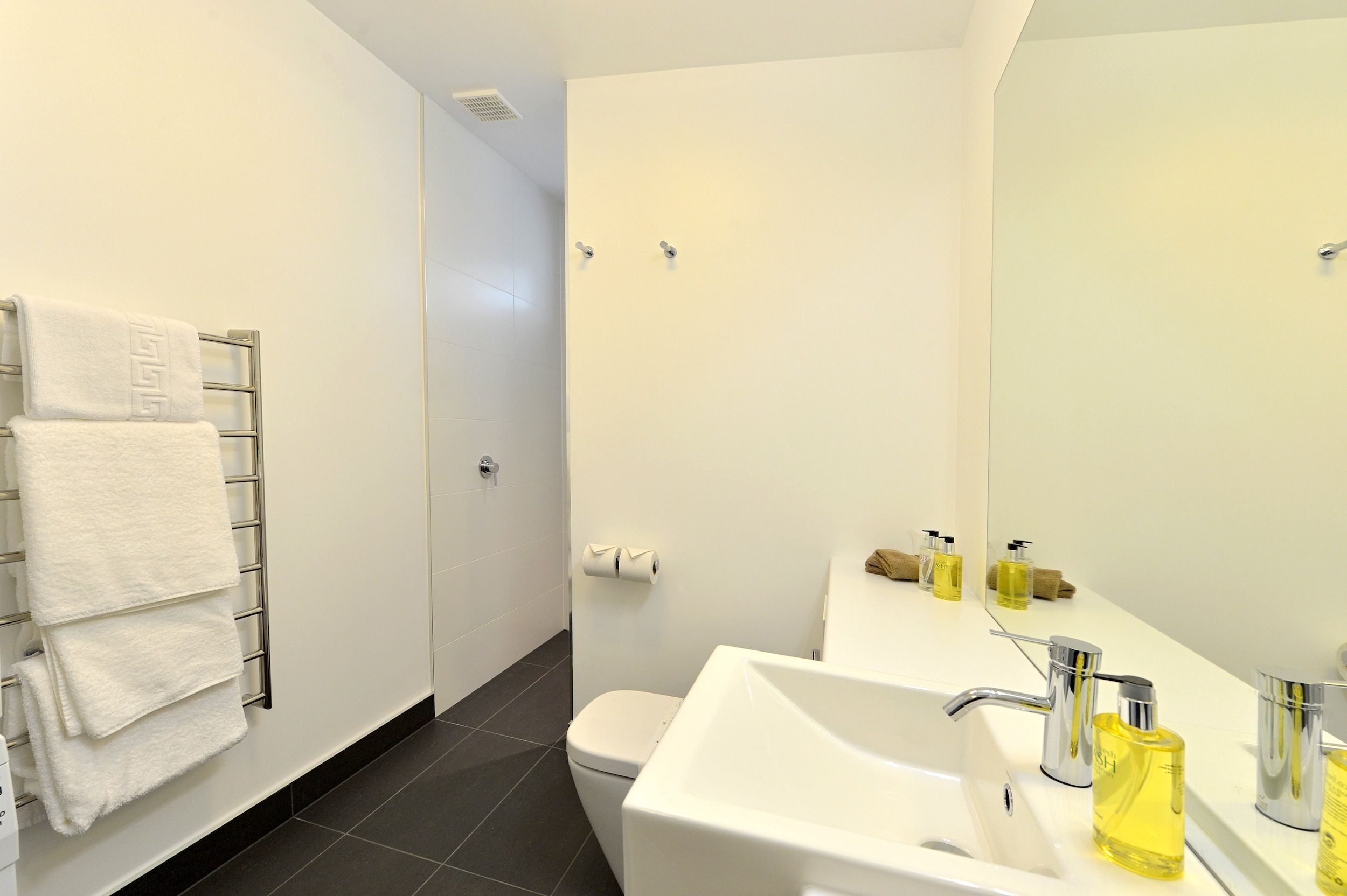 Un baño moderno con lavamanos, espejo y perchero blancos.