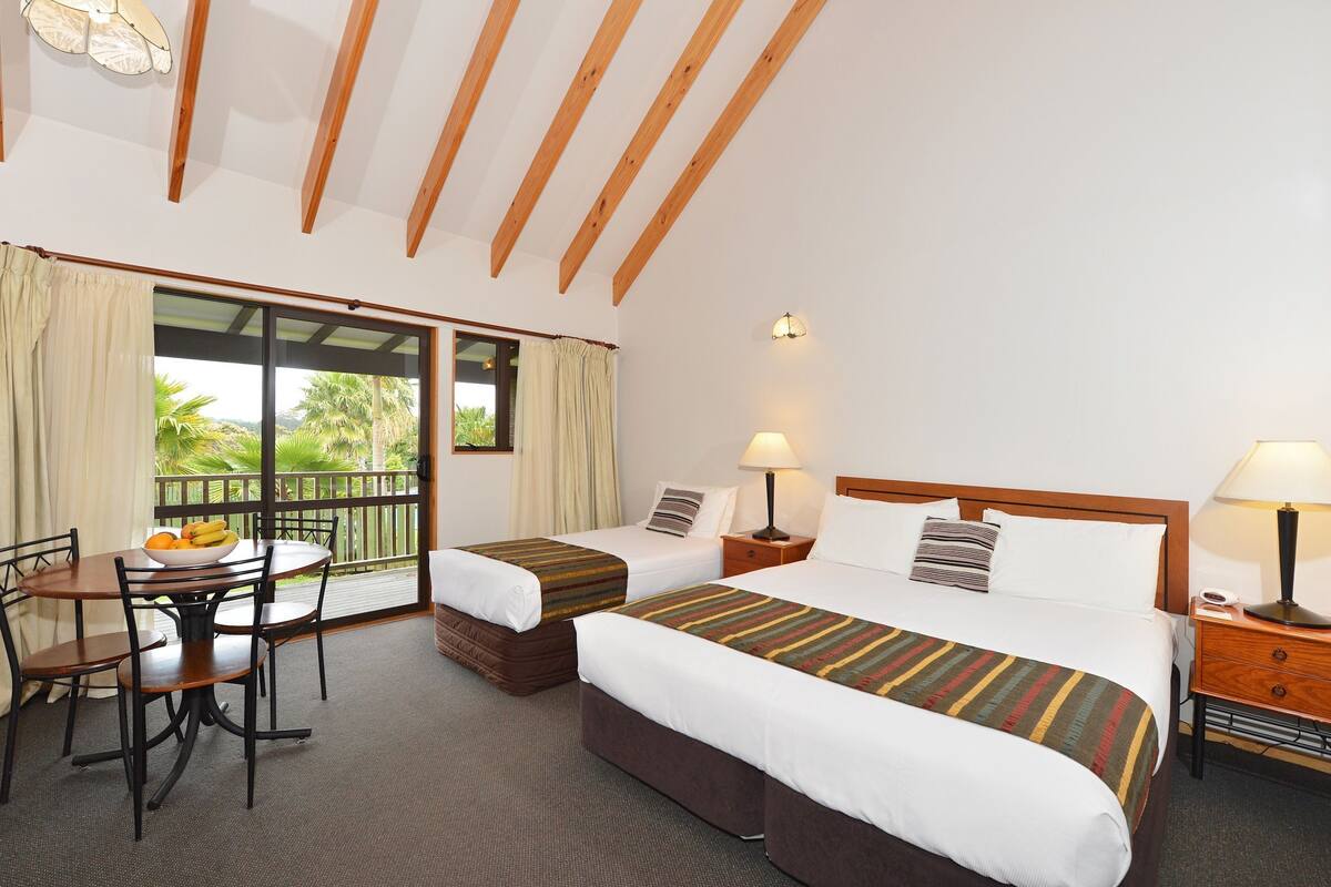 Een hotelkamer met twee bedden, een eettafel en een balkon met gordijnen.