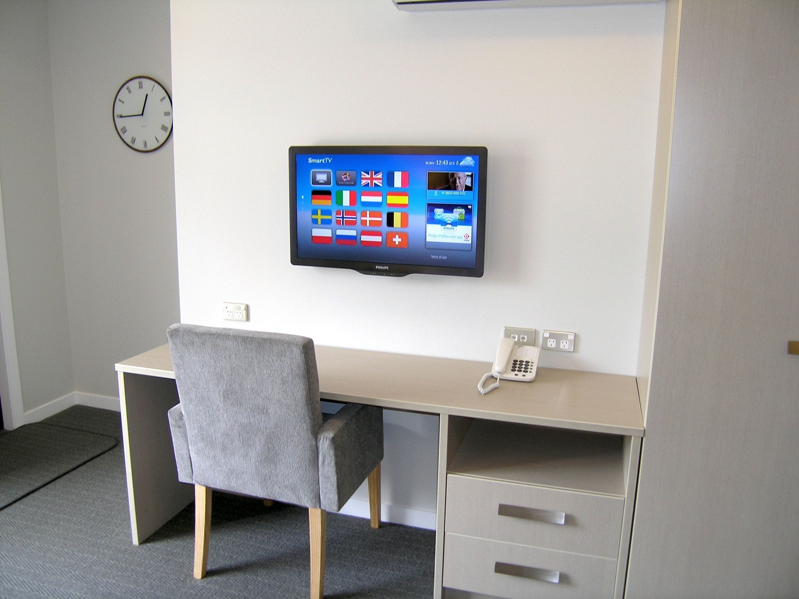 Um espaço de escritório moderno com uma mesa, uma cadeira e uma TV de tela plana fixada na parede, exibindo vários aplicativos.