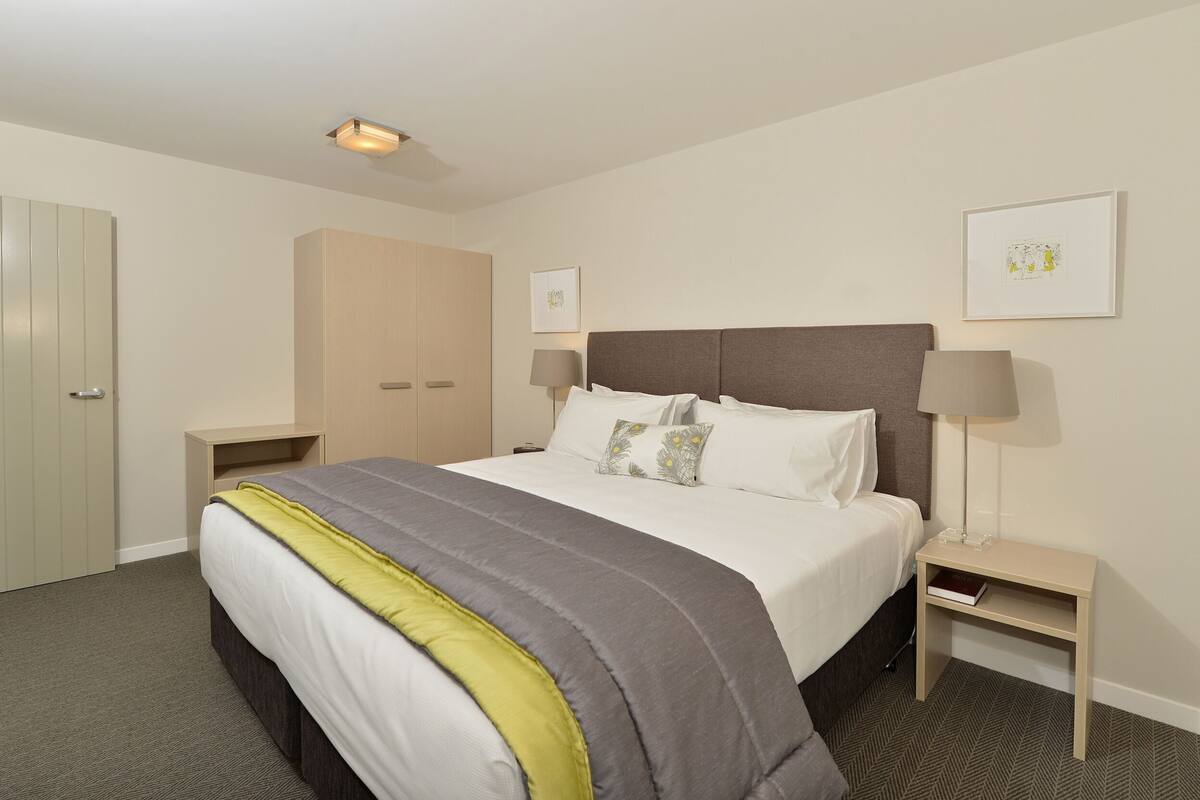 Een hotelkamer met een bed, nachtkastjes, een garderobe en kunst aan de muren.