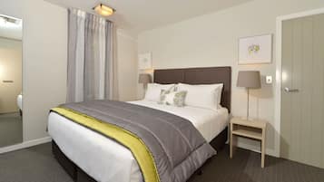 A neatly arranged hotel room with a large bed, bedside lamps, a mirror, and a door.